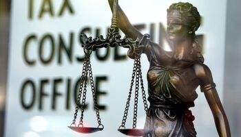 Statue of Justice with blindfolded eyes and balance in hand in front of a sign that reads Tax Consulting Office.