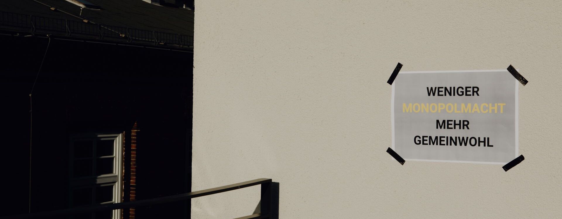 A sheet of paper is stuck to a white house wall with the words Less monopoly power, more common good